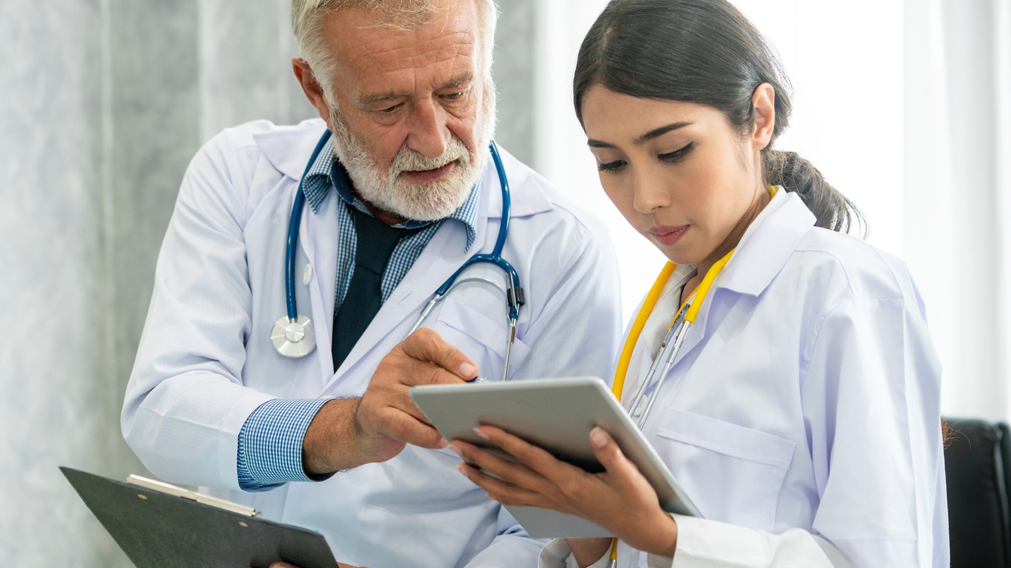 Senior male doctor using tablet computer while discussing with another doctor at the hospital. Medical healthcare staff and doctor service.